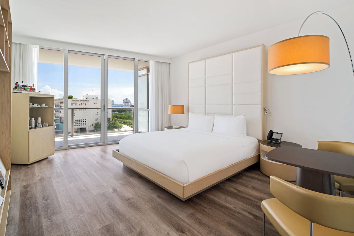 Een moderne hotelkamer met een groot bed, een bureau en een stoel. De kamer heeft een groot raam met uitzicht op de stad.