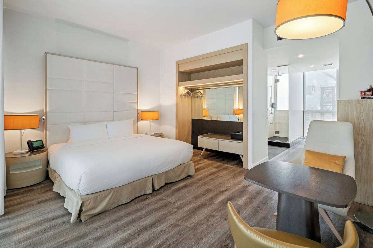 Een hotelkamer met een groot bed, nachtkastjes met lampen, een bureau met stoel, een spiegel en een douche.