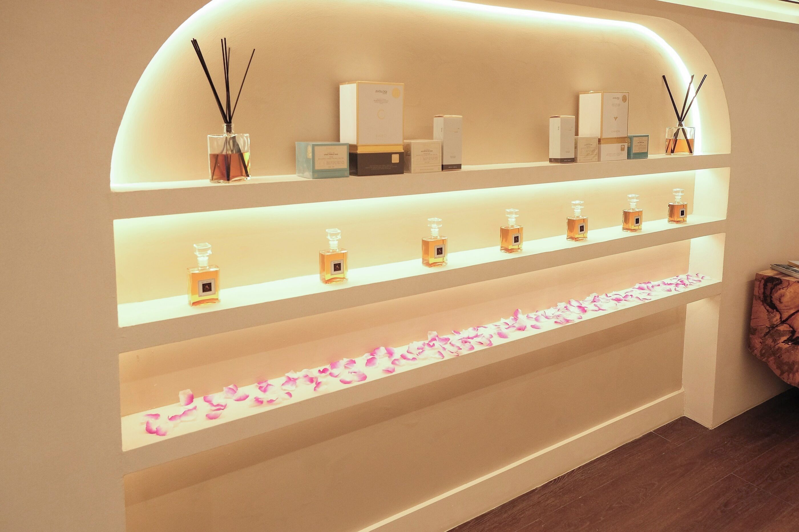 A display of various scented products on shelves with a decorative arrangement of rose petals at the bottom.