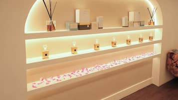 A display of various scented products on shelves with a decorative arrangement of rose petals at the bottom.