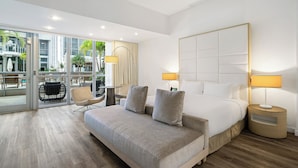 A modern hotel room with a large bed, two bedside tables with lamps, a sofa, and a view of the outdoor area through large glass doors. - The Grayson Miami Downtown (Miami)