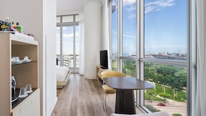 A modern hotel room with a large window, a sofa, a table, and a TV. - The Grayson Miami Downtown (Miami)