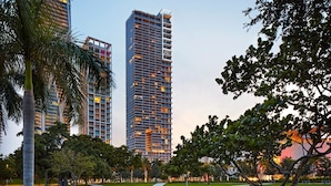 A modern high-rise building with a central atrium and multiple balconies, surrounded by a well-maintained park with pathways and trees. - The Grayson Miami Downtown (Miami)