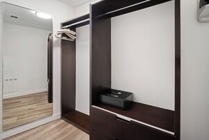 A walk-in closet with a mirrored closet door, a dark wooden wardrobe, and a black box on the lower shelf.