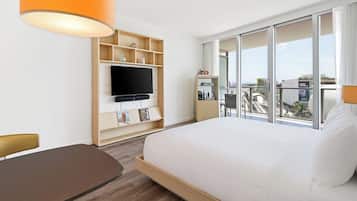 Ein Hotelzimmer mit Bett, Fernseher, einer Holzablage mit Gegenständen, einem Balkon mit Aussicht und einem Tisch.