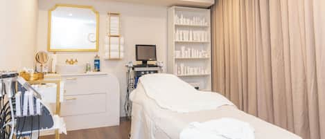 A clinical setting with a treatment bed, medical equipment, and a shelf with various bottles.