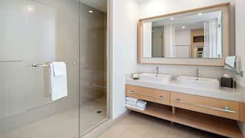 Un baño moderno con cabina de ducha de vidrio, dos lavamanos, un espejo grande y un mueble de tocador de madera.