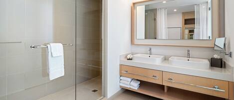 Un baño moderno con cabina de ducha de vidrio, dos lavamanos, un espejo grande y un mueble de tocador de madera.