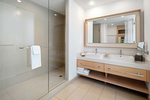 A modern bathroom with a glass shower enclosure, two sinks, a large mirror, and a wooden vanity. - The Grayson Miami Downtown (Miami)
