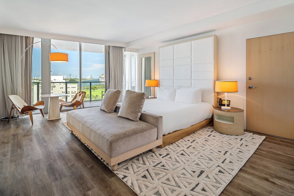 Een moderne hotelkamer met een groot bed, een zithoek met stoelen, uitzicht op de stad en een balkon.