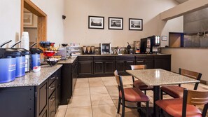 A kitchen with a granite countertop, black cabinets, a dining table with chairs, and a coffee machine.