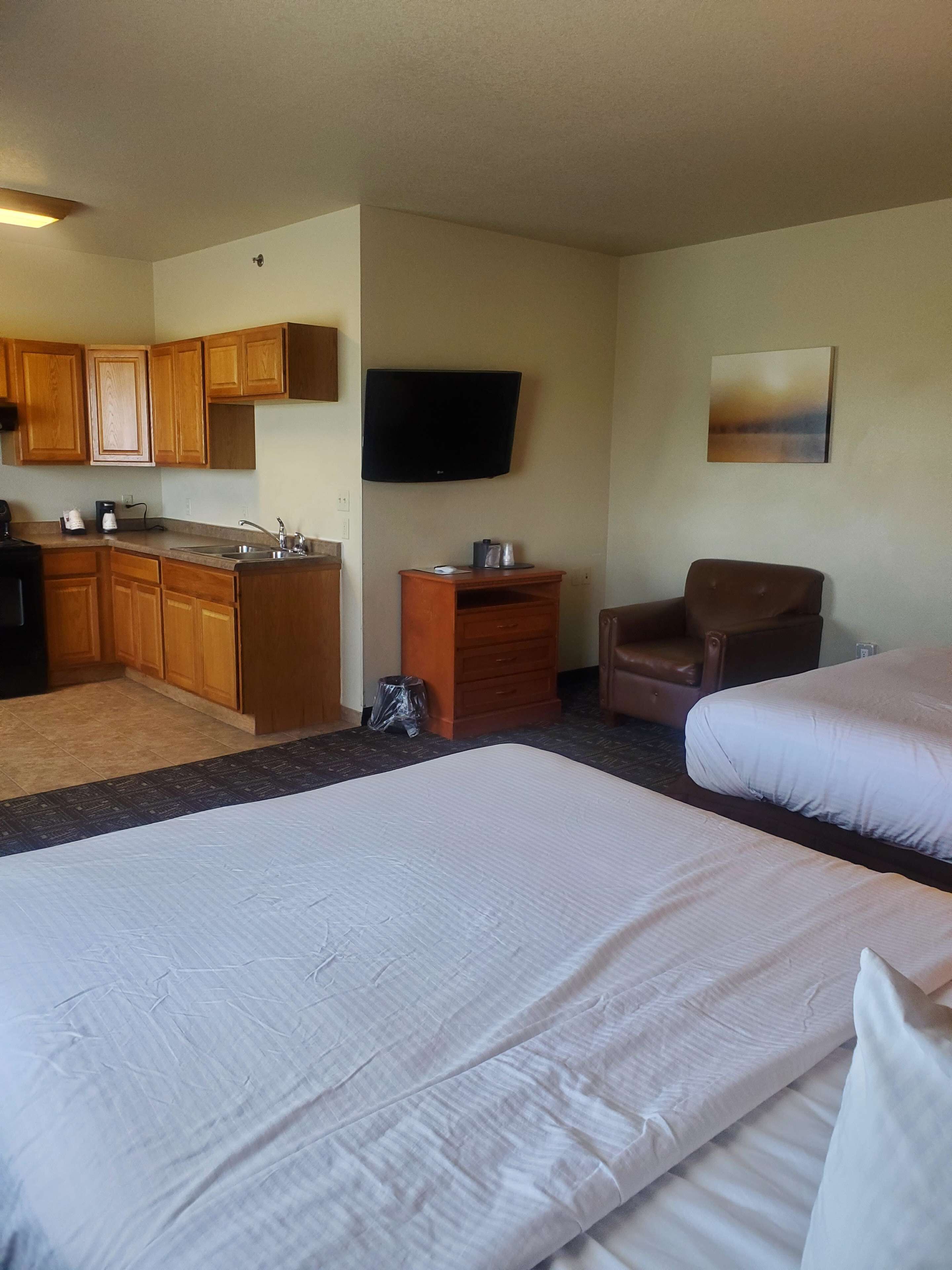 Habitación de hotel con kitchenette, televisor de pantalla plana, un sillón marrón y dos camas.