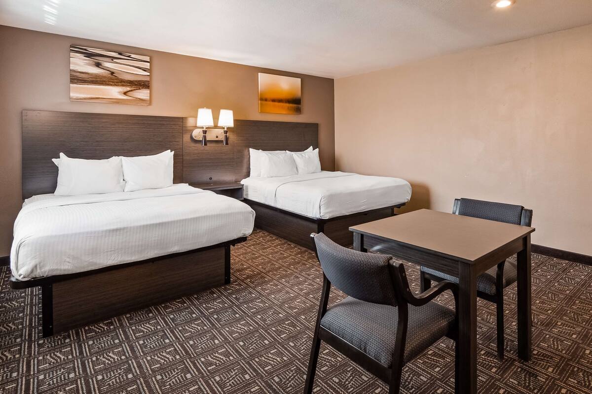 Habitación de hotel con dos camas, una mesa y una silla. Hay lámparas de pared y cuadros sobre las camas.
