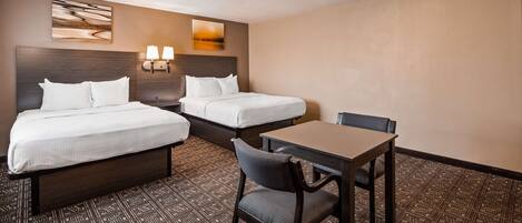 Habitación de hotel con dos camas, una mesa y una silla. Hay lámparas de pared y cuadros sobre las camas.