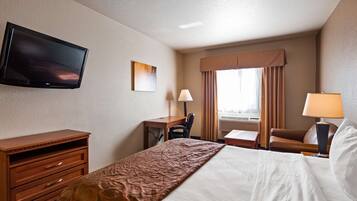 Habitación de hotel con cama, escritorio, silla, televisión y ventana con cortinas.