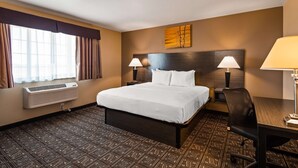 A hotel room with a large bed, two bedside lamps, a desk with a chair, a window with curtains, an air conditioning unit, and a wall art piece. - Best Western Rambler (Walsenburg)