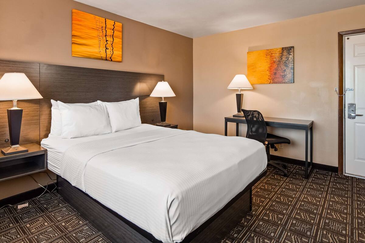Habitación de hotel con una cama grande, dos lámparas de noche, un escritorio con silla y obras de arte en las paredes.
