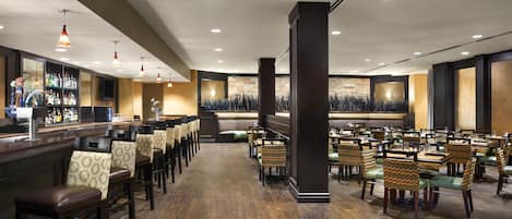 A hotel lobby with a bar area, seating arrangements, and a central pillar.