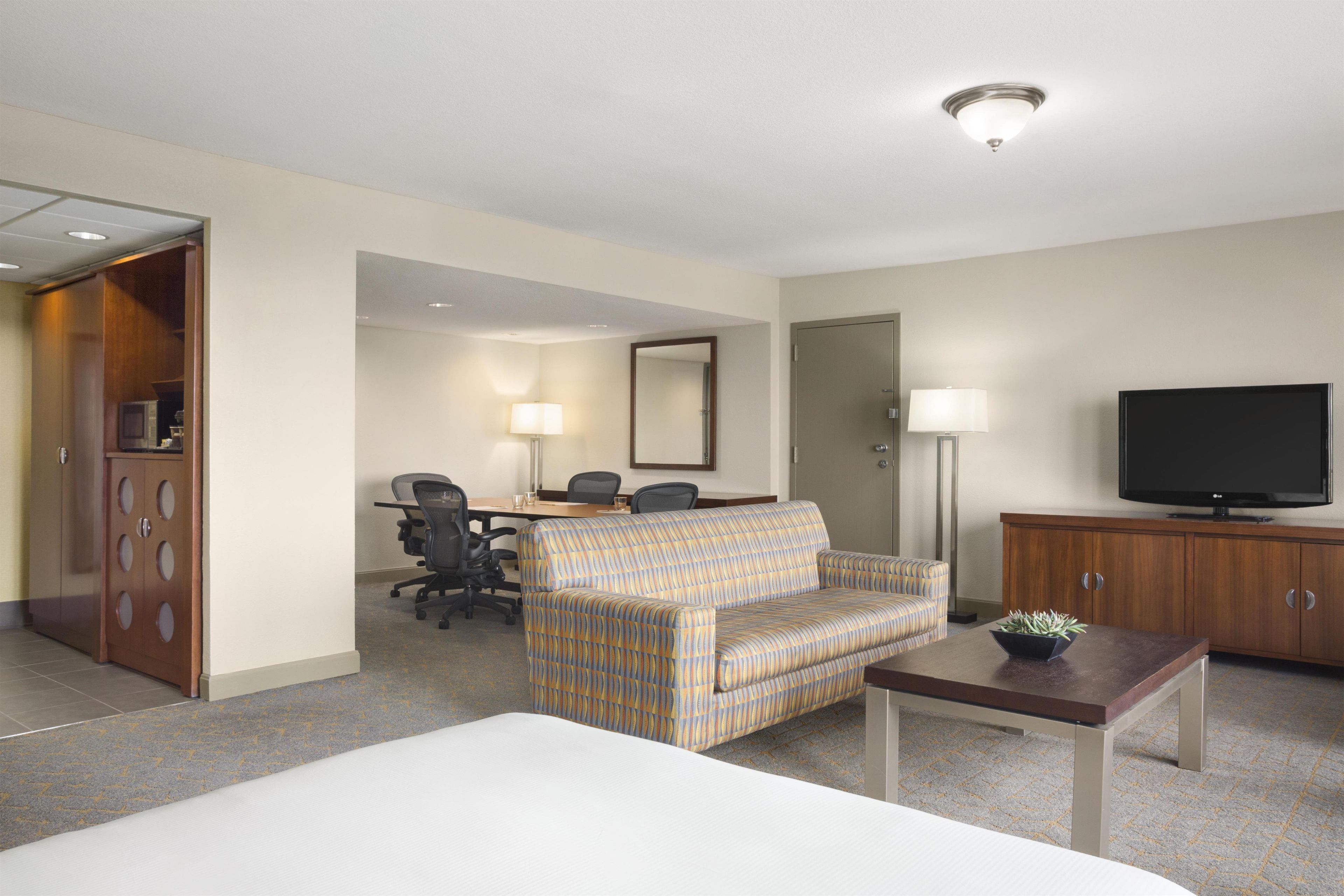 A hotel room with a bed, a sofa, a desk with a chair, a television, and a cabinet.