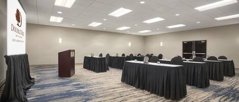 A conference room with a podium, tables, chairs, and a carpeted floor.