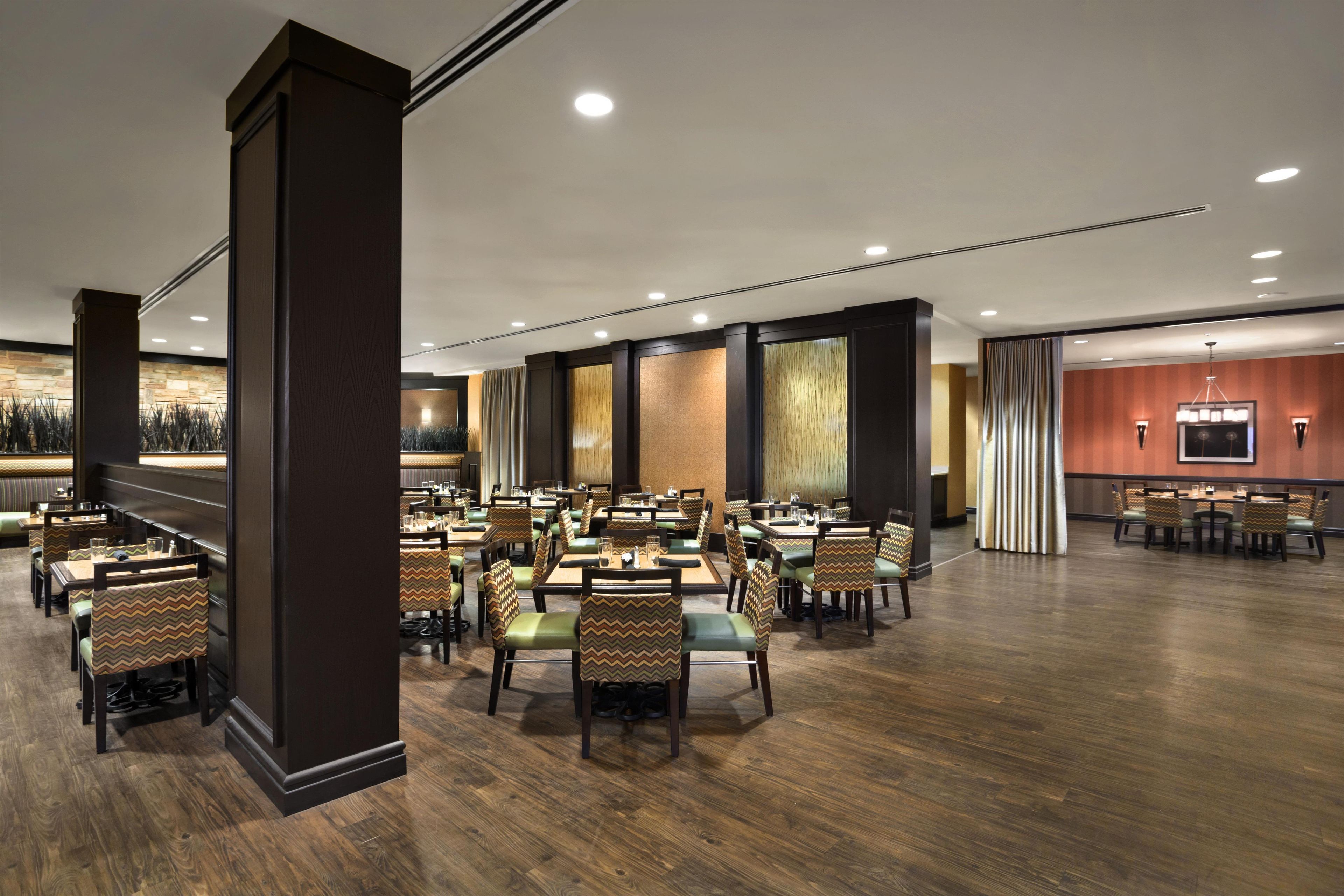 A spacious dining area with multiple tables and chairs, wooden flooring, and a modern ceiling design.