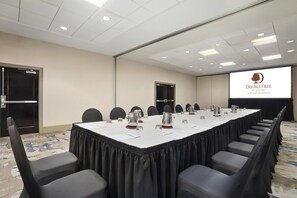 A conference room with a long table, chairs, a projector screen, and a door. - DoubleTree by Hilton Dallas - DFW Airport North (Irving)