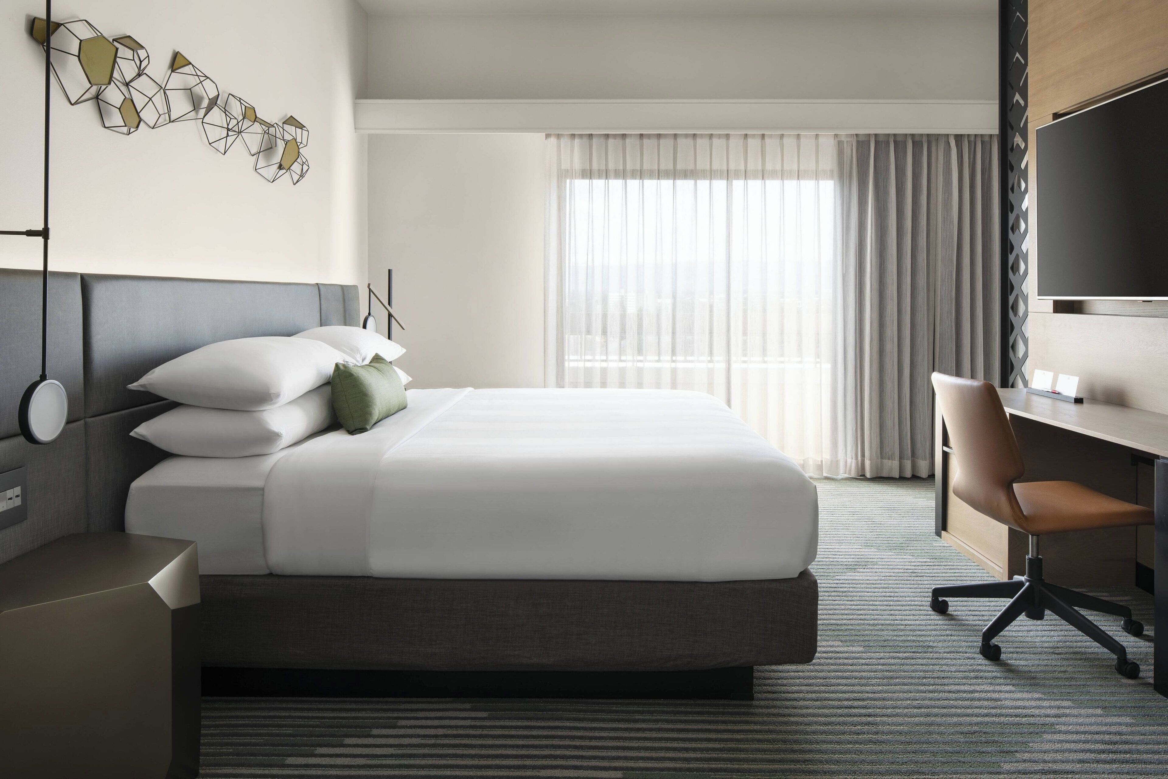 A hotel room with a bed, a desk, a chair, and a TV.