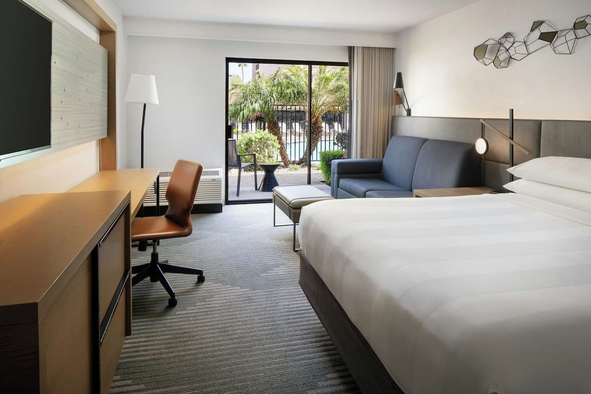 A hotel room with a large bed, a desk with a chair, a sofa, a small table, and a view of the outside.