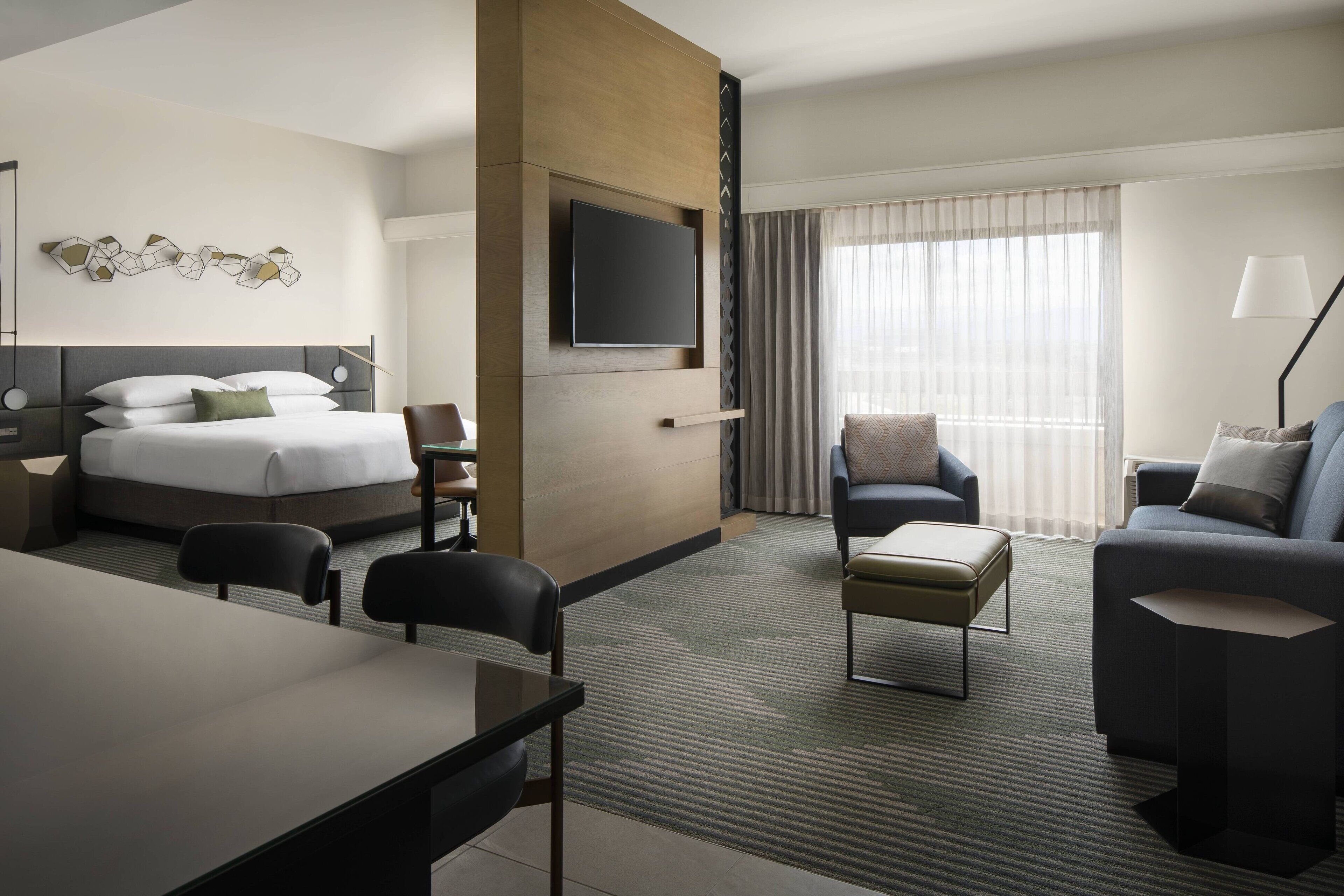 A hotel room with a bed, a desk, a sofa, and a TV mounted on the wall.