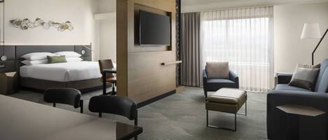 A hotel room with a bed, a desk, a sofa, and a TV mounted on the wall.