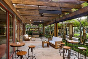 An outdoor seating area with wooden tables and chairs, a sofa, and a bar area with a counter and stools.