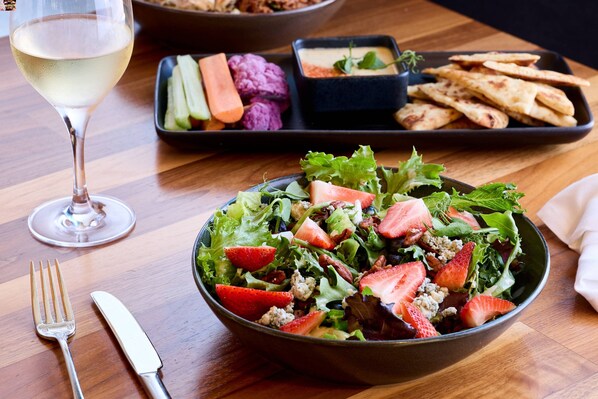 A dining table with a salad, a glass of white wine, and a plate of flatbread.