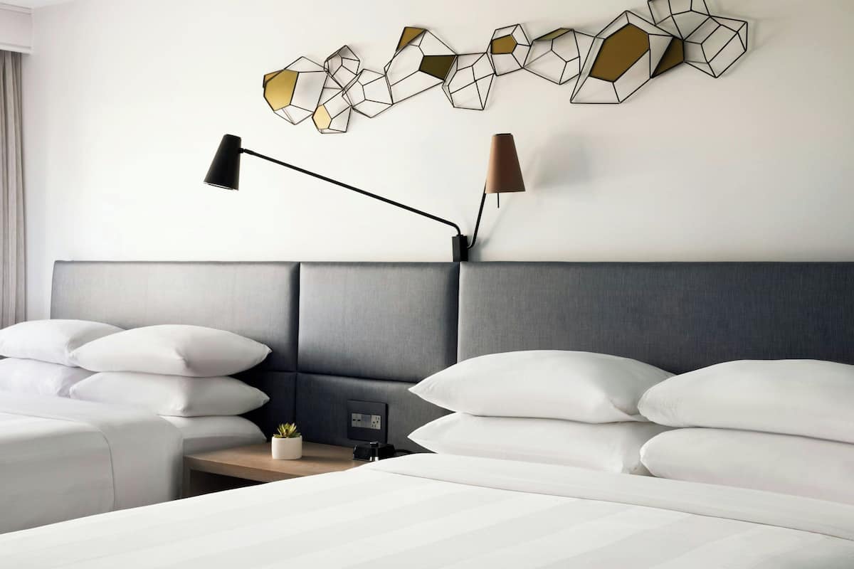 A modern hotel room with a large bed, two bedside tables, a wall-mounted lamp, and a geometric wall art piece.