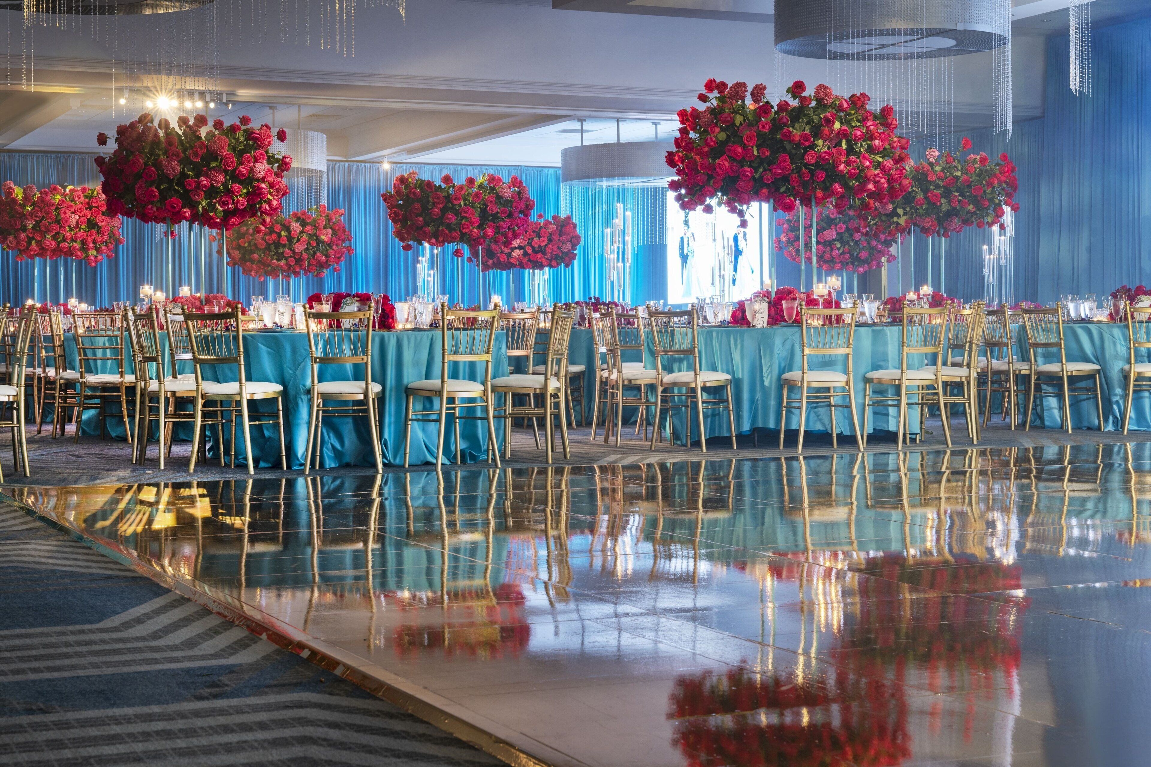 A banquet hall with tables set for a formal event, featuring reflective flooring and blue drapery.