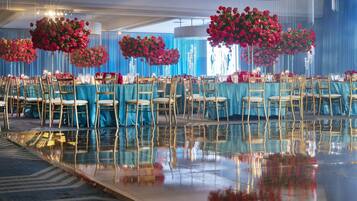 A banquet hall with tables set for a formal event, featuring reflective flooring and blue drapery.