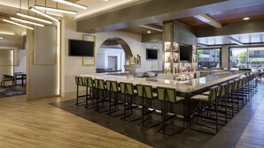 A modern bar area with a long counter, multiple bar stools, and a television screen. - Santa Clara Marriott (Santa Clara)