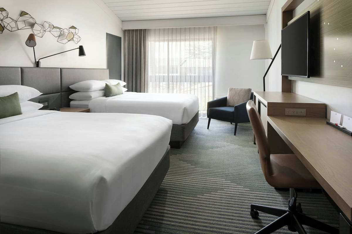 A hotel room with two beds, a desk, a chair, a TV, and a window with curtains.