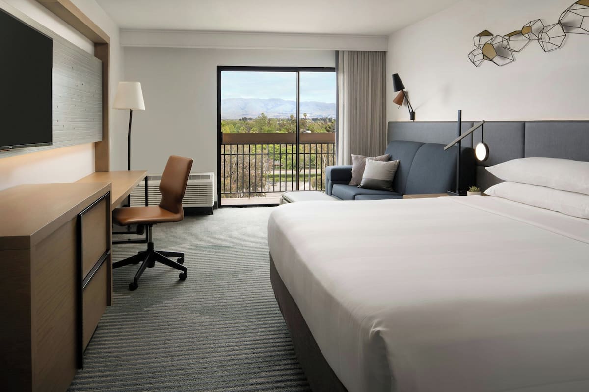 A hotel room with a bed, desk, chair, and a view of the outdoors.
