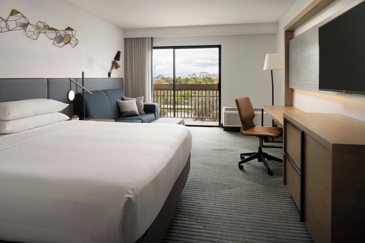 Une chambre d’hôtel avec un grand lit, un bureau, une chaise et un balcon donnant sur la ville.