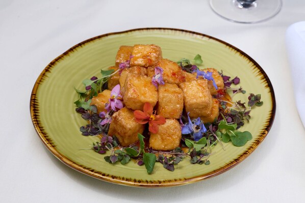 Une assiette de nourriture contenant des cubes de tofu et des fleurs comestibles, le tout présenté sur une assiette en céramique verte.