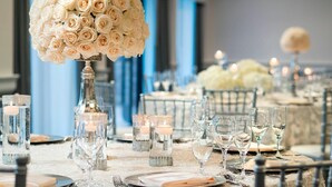 A formal dining table with a large floral centerpiece, candle holders, and neatly arranged cutlery. - Santa Clara Marriott (Santa Clara)
