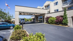 A hotel entrance with a covered walkway, parking area, and flag display.