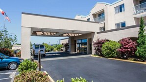 A hotel entrance with a covered walkway, a parking lot, and a flag. - Quality Inn Grand Suites Bellingham (Bellingham)