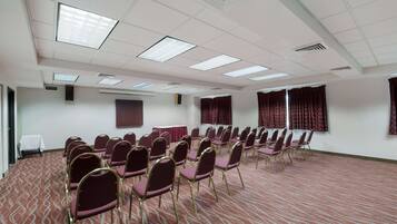 A conference room with rows of chairs, a carpeted floor, and a ceiling with fluorescent lights.
