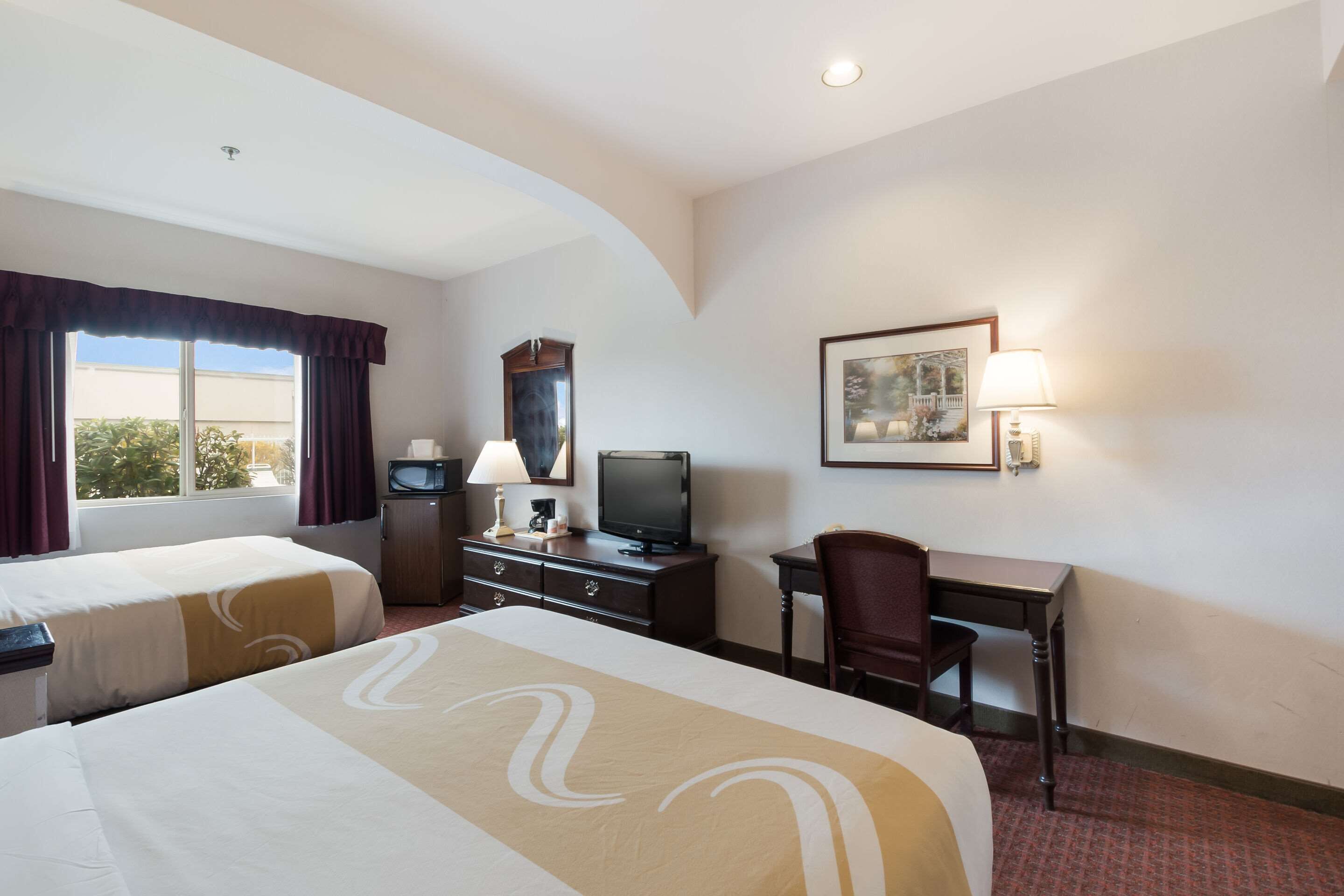 Habitación de hotel con dos camas, un escritorio, un televisor, una lámpara y un cuadro en la pared.