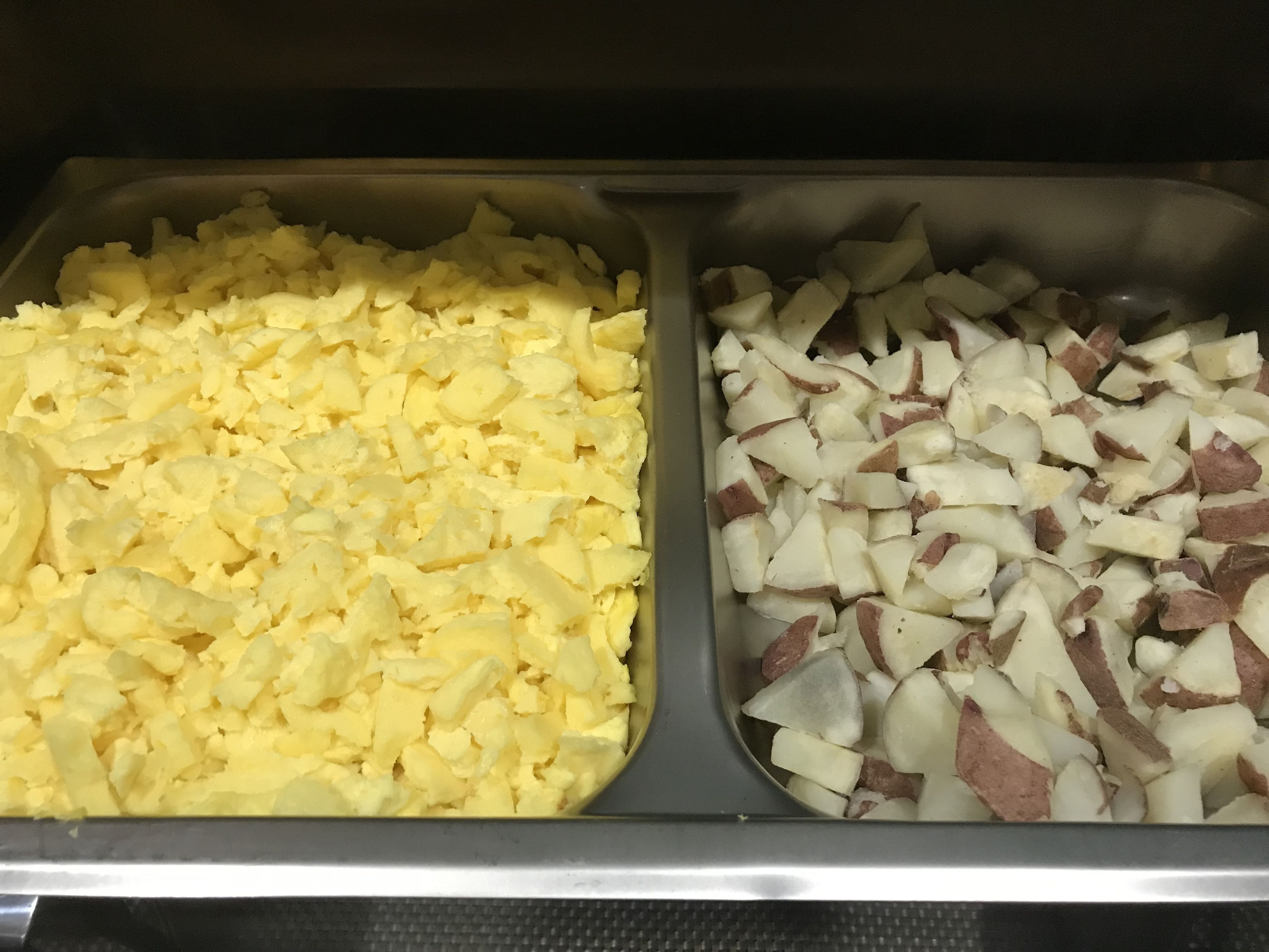 Two metal trays filled with diced potatoes and eggs.