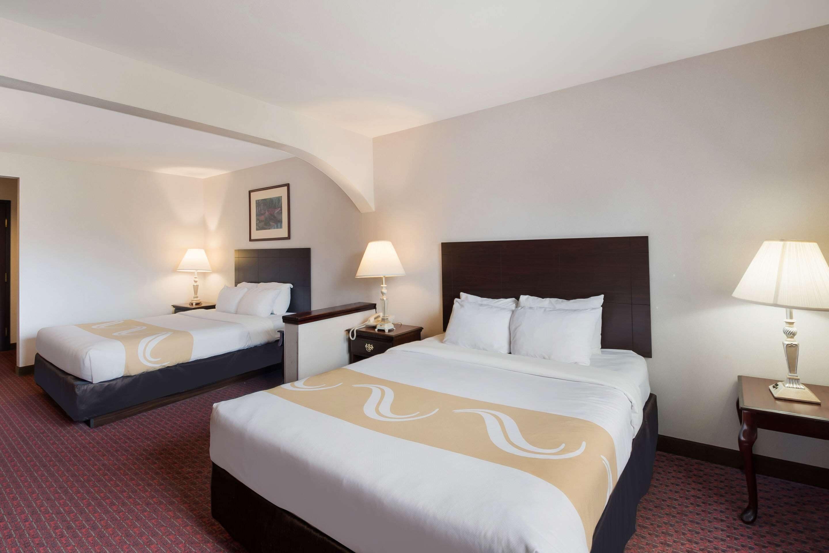A hotel room with two beds, each with a headboard, bedside tables, lamps, and a framed picture on the wall.