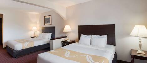 A hotel room with two beds, each with a headboard, bedside tables, lamps, and a framed picture on the wall.