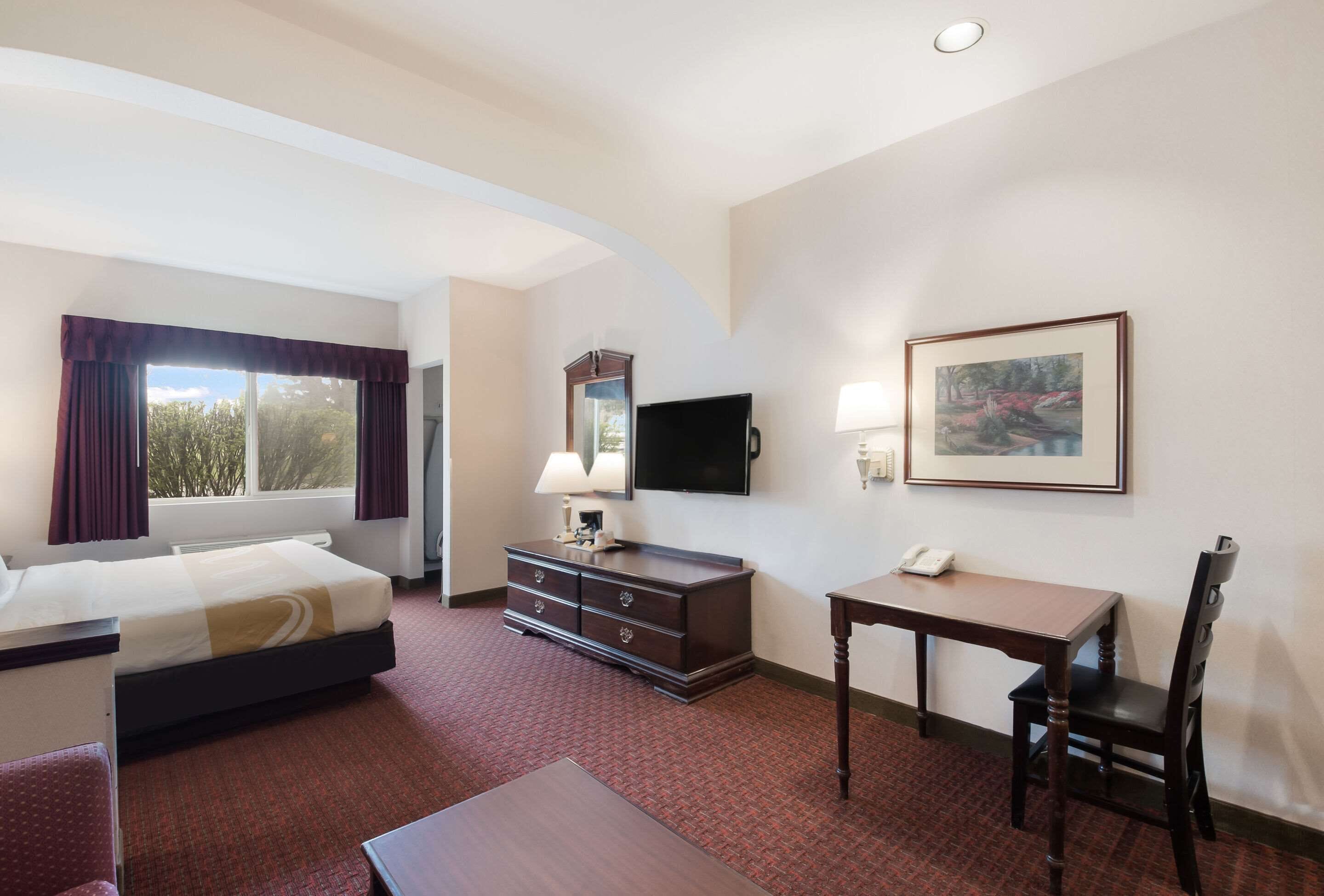 A hotel room with a bed, a desk, a chair, a dresser, a television, and a painting on the wall.