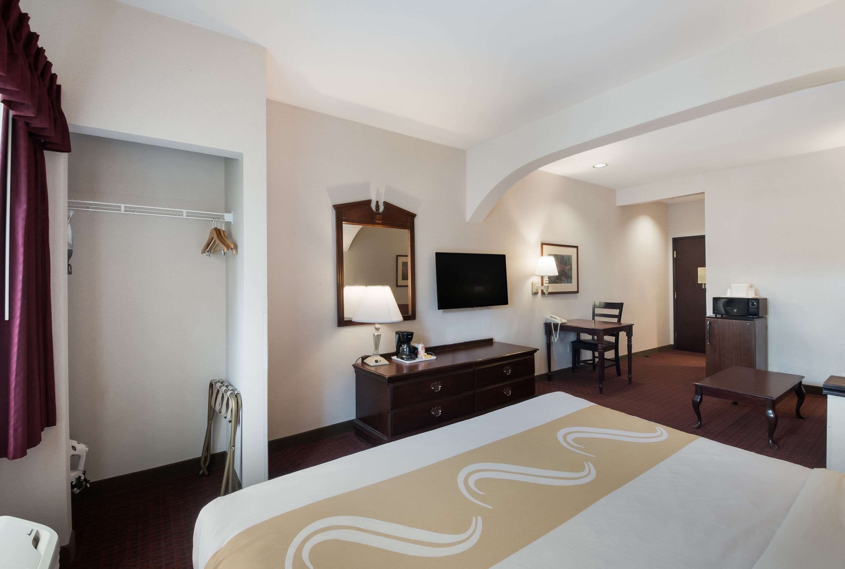 Habitació d'hotel amb llit, escriptori, cadira, televisió, mirall i armari.
